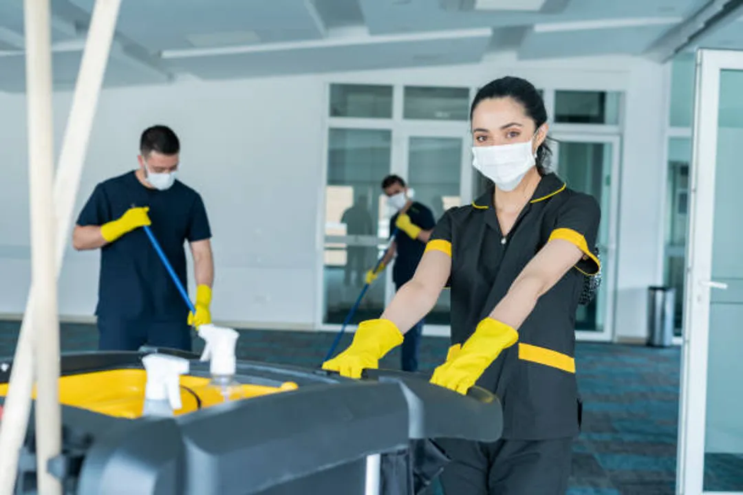 Uniformed cleaning crew with gloves and a supply cart working in an office building