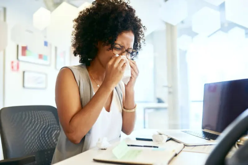 african american female at desk sneezing from allergies